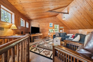 Interior acogedor de una cabaña con techo de madera, televisor, sofá y alfombra.