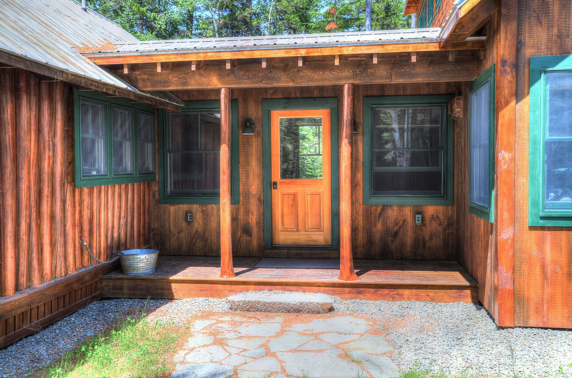 A wooden cabin with a front porch, a wooden door, and two windows with green frames.