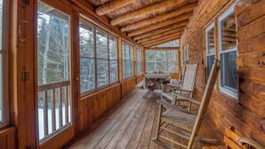 Eine Blockhütte mit einer Holzdiele, großen Fenstern und einem Tisch mit Stühlen.