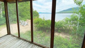 Eine Holzterrasse mit einem großen Fenster mit Blick auf einen See und viel Grün.