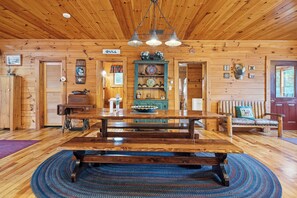 A wooden interior with a large dining table, a bench, and a hanging light fixture.
