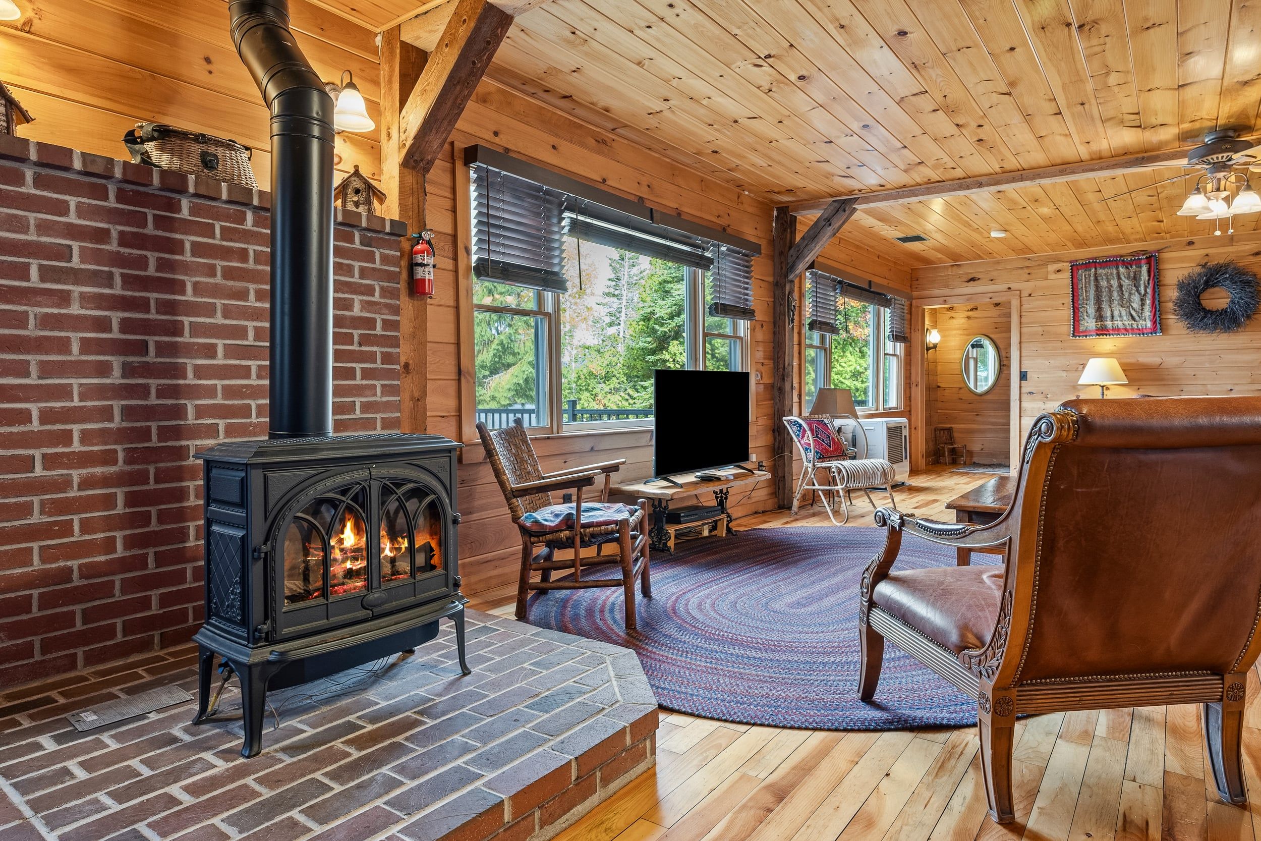 A cozy cabin interior with a fireplace, wooden furniture, and large windows.