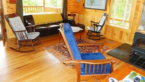 L’intérieur d’un chalet accueillant, avec un plancher en bois, un fauteuil bleu rembourré, un fauteuil à bascule, un canapé et une cheminée.