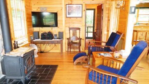 L’intérieur chaleureux d’un chalet avec un poêle à bois, un téléviseur et un coin repas doté de chaises bleues.
