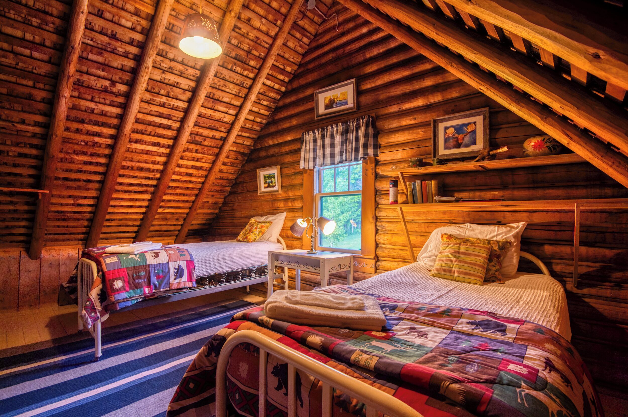 Een gezellig slaapkamer onder de pannen met twee bedden, een raam met gordijnen en houten wanden.