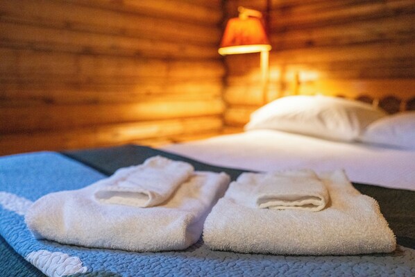 A cozy room with a bed, a lamp, and neatly folded towels on a bedspread.