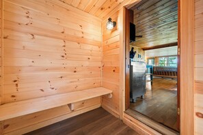 A wooden cabin interior with a bench, a wall-mounted light, and a view of a wooden deck outside.