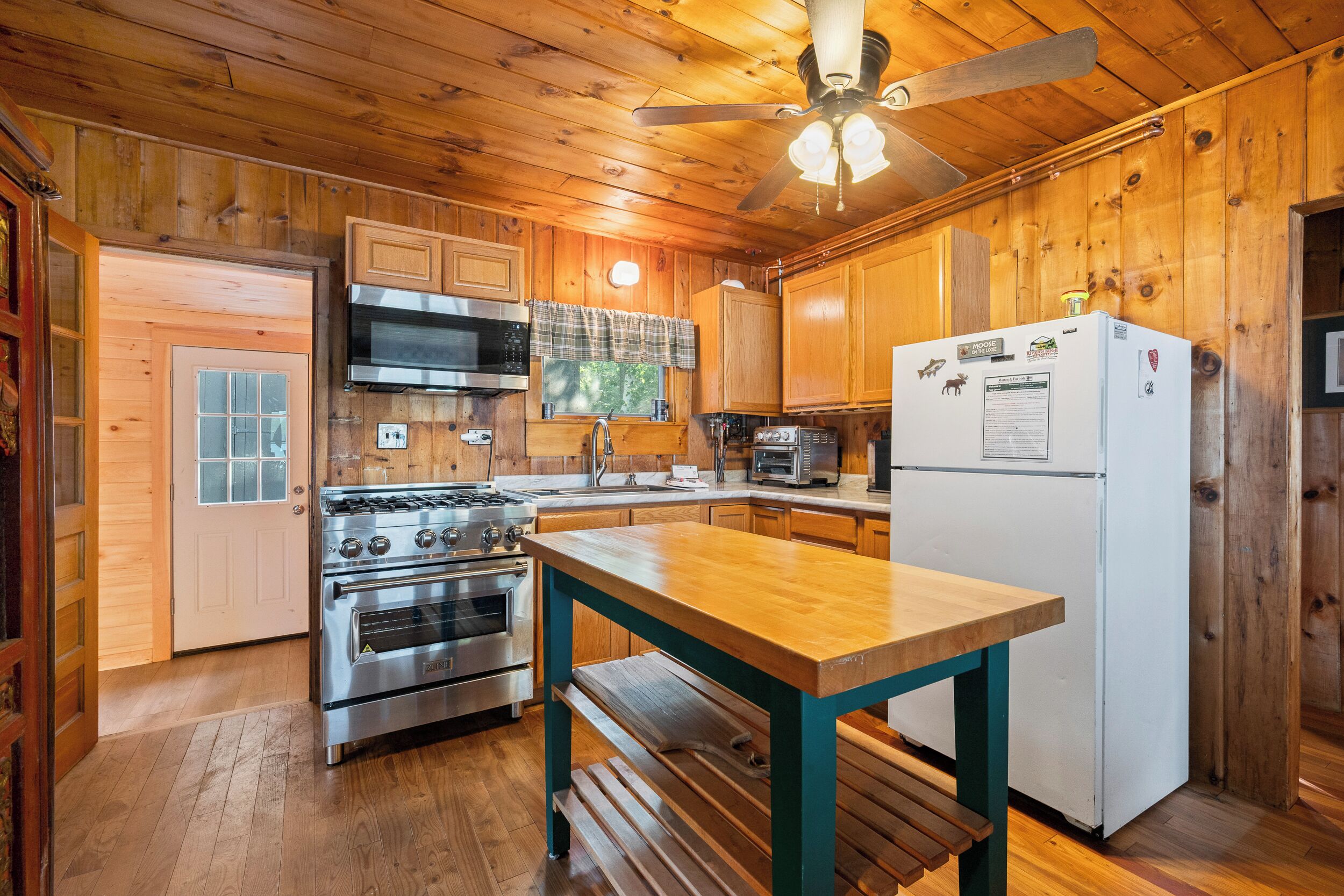 A wooden cabin kitchen with a gas stove, oven, microwave, and a refrigerator.