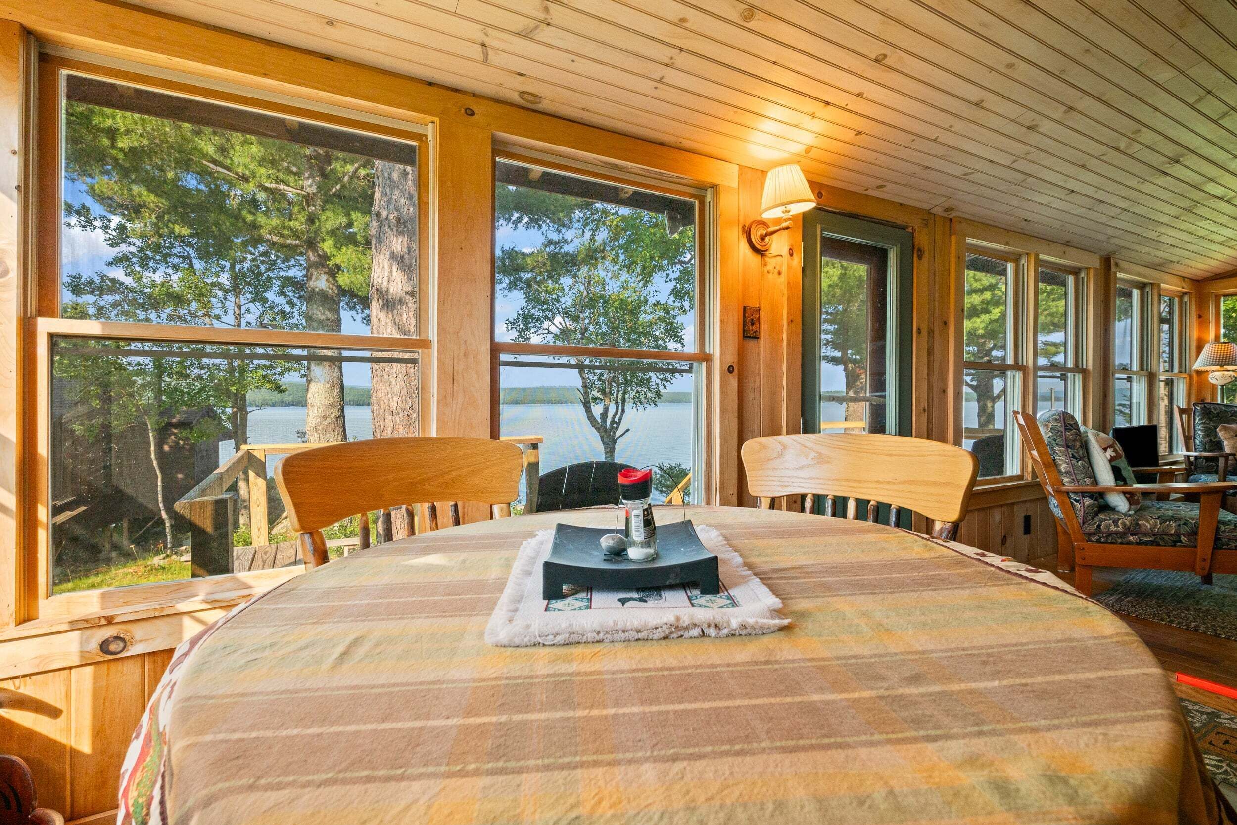 Una habitación con un ventanal grande con vista a un lago, una mesa con camino de mesa y una silla.