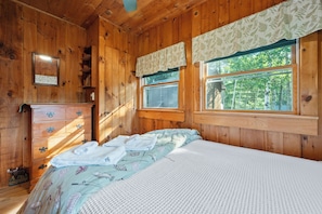 Habitació de cabana de fusta amb un llit, una petita taula de nit i finestres.