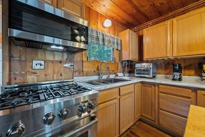 A kitchen with wooden cabinets, a stainless steel stove, a sink, and a coffee maker. - Four Loons | Waterfront | Pet Friendly (Oquossoc)