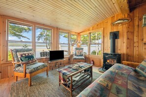 Interior acogedor de una cabaña con paredes de madera, ventanas amplias, chimenea y televisor.