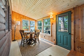 A log cabin interior with a dining area, wooden walls, and a green door.