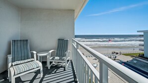 Un balcon avec deux chaises à rayures, une petite table et une vue sur la plage et l’océan.