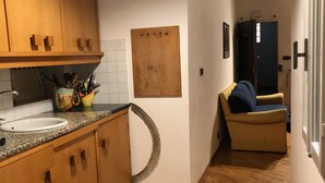 A narrow hallway with wooden flooring, a kitchen area with wooden cabinets, a sink, and a wall-mounted corkboard. - Macci Number Eight (Florence)