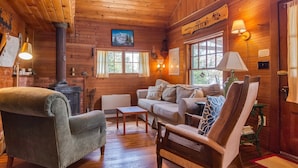 A cozy cabin interior with wooden walls, a fireplace, a sofa, and a chair. - 🐾Gray Wulff - This rustic dog friendly camp sits on the shore of Quimby Pond (Rangeley)