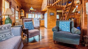 A cozy cabin interior with wooden floors, a staircase to a loft, a dining area, and a living room with two sofas and patterned cushions. - 🐾Gray Wulff - This rustic dog friendly camp sits on the shore of Quimby Pond (Rangeley)