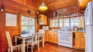 A wooden cabin interior with a dining table, chairs, a kitchen with a stove, microwave, and cabinets. - 🐾Gray Wulff - This rustic dog friendly camp sits on the shore of Quimby Pond (Rangeley)