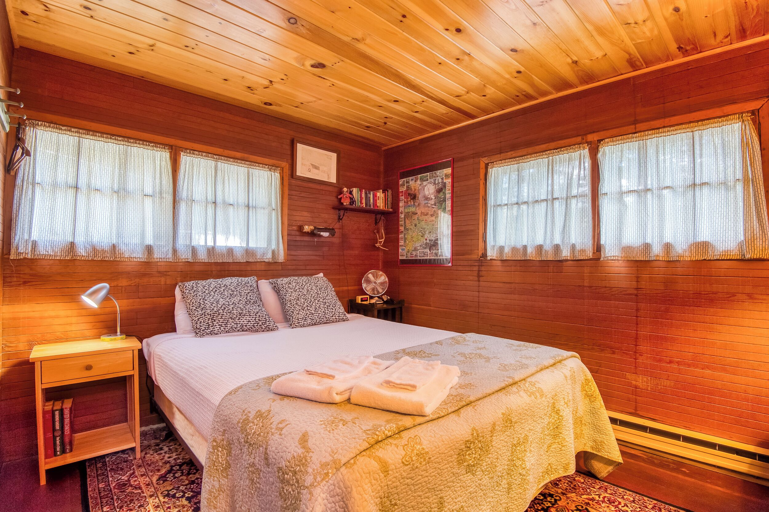 Ein Schlafzimmer mit Holzwänden, einem Bett, einem Nachttisch und einem kleinen Regal mit Büchern.
