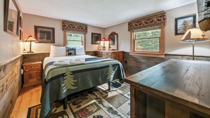 Une chambre à coucher avec un lit, des tables de chevet en bois, un bureau et une fenêtre donnant sur un paysage verdoyant.