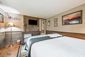 A hotel room with a bed, a television, a wooden cabinet, and a painting on the wall. - Rangeley Manor 7 | Cozy Cottage with Shared Access to Rangeley Lake (Rangeley)