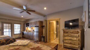 A bedroom with two beds, a ceiling fan, a kitchen area, and a bathroom. - Oquossoc Suite #5 | A/C (Oquossoc)
