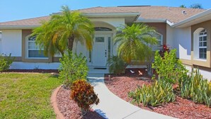 A residential house with a front porch, palm trees, and a landscaped garden.