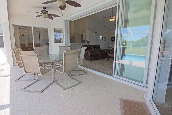 A modern interior with a glass dining table, chairs, ceiling fans, and a view through large sliding glass doors.