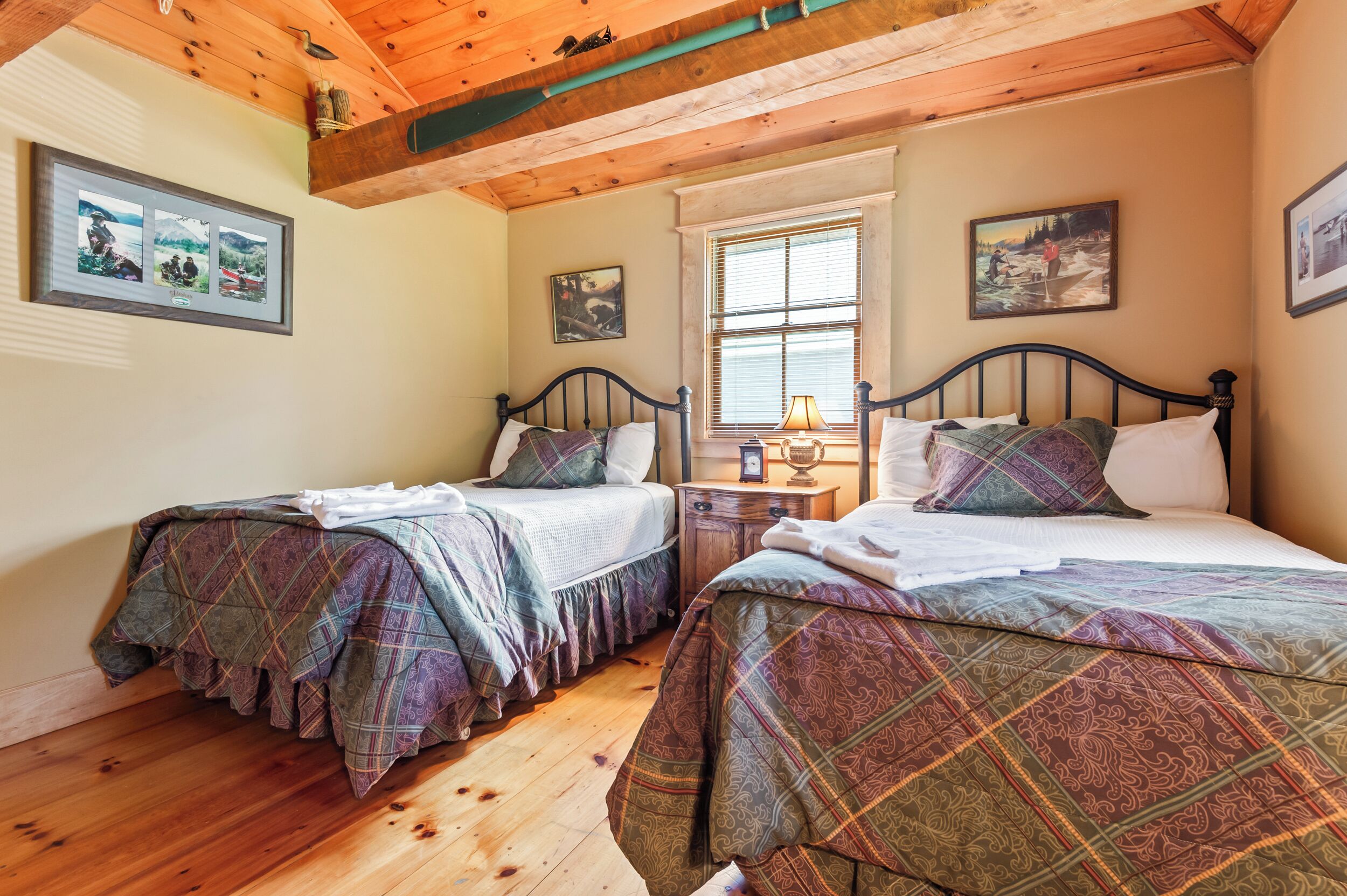 Ein Schlafzimmer mit zwei Betten, Holzboden, einem Fenster mit Jalousien und Wandbildern.