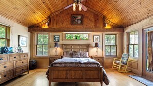 Un dormitorio con paneles de madera, una cama, un aparador y un sillón mecedora.