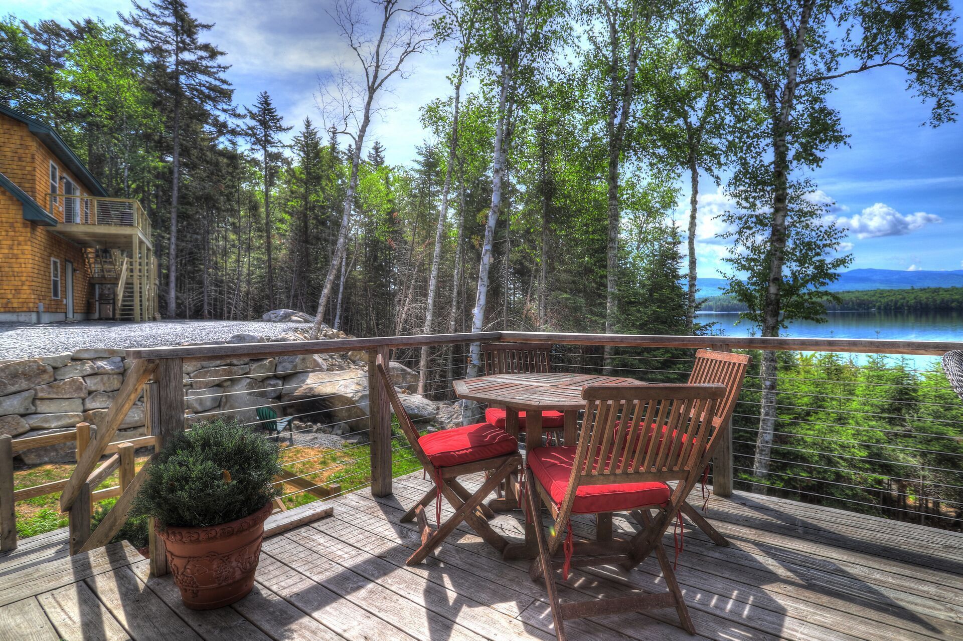A wooden deck with a table and chairs, overlooking a lake and forest.