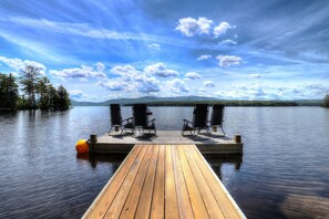 Une jetée en bois s’avançant dans une étendue d’eau calme, avec deux fauteuils à bascule et une bouée jaune.