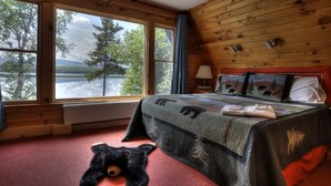 A bedroom with a large window, a bed with a quilt, a teddy bear, and a lamp. - Beach Front Retreat - Private home on Mooselookmeguntic Lake (Oquossoc)