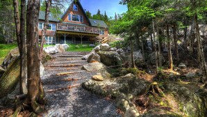 A rustic cabin with a stone staircase leading to a porch, surrounded by a forest. - Beach Front Retreat - Private home on Mooselookmeguntic Lake (Oquossoc)