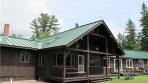 A wooden cabin with a porch and a green roof, surrounded by trees. - Saddleback Lake Lodge 25 | Close to Saddleback (Rangeley)