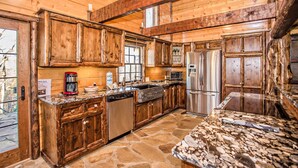 A rustic kitchen with wooden cabinets, a stone floor, and a granite countertop. - 🌲 Bird's Perch View 🌅 Custom Cabin, Mountain Views, Hot Tub & Fire Pit (Sevierville)