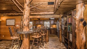 A rustic interior with a stone floor, wooden furniture, and a large tree stump centerpiece. - 🌲 Bird's Perch View 🌅 Custom Cabin, Mountain Views, Hot Tub & Fire Pit (Sevierville)