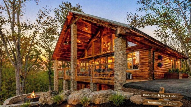 A log cabin with multiple windows, a stone foundation, and a fire pit. - 🌲 Bird's Perch View 🌅 Custom Cabin, Mountain Views, Hot Tub & Fire Pit (Sevierville)