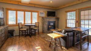 A cozy interior with a stone fireplace, wooden furniture, and large windows. - Oquossoc Suite #6 | A/C & Fireplace (Oquossoc)