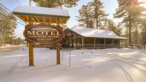 A motel sign with a pet-friendly notice, surrounded by snow-covered ground and trees. - Oquossoc Suite #6 | A/C & Fireplace (Oquossoc)