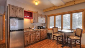 A kitchen with wooden cabinets, a stainless steel refrigerator, a microwave, and a dining table with chairs. - Oquossoc Suite #6 | A/C & Fireplace (Oquossoc)