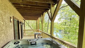 Een hottub in een overdekte buitenruimte met houten balken en uitzicht op bomen.