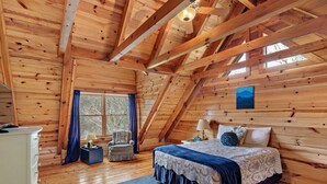 Een knus houten slaapkamer met een bed, een stoel, een dressoir en een raam met gordijnen.