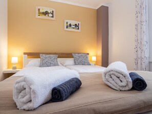 Une chambre d’hôtel avec deux lits, chacun doté d’une tête de lit, de draps blancs et de deux oreillers. On y trouve deux lampes de chevet et deux tableaux accrochés au mur.