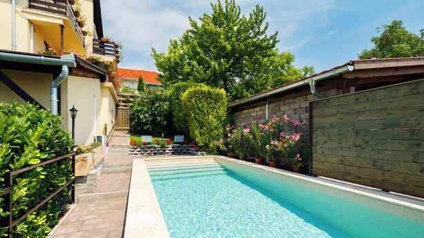 A swimming pool with a tiled deck, surrounded by a wooden fence and potted plants. - Casa Montana II- Country Apartment (Balatonalmadi)