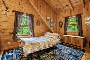 A wooden cabin bedroom with a bed, a bench, and a window with curtains.