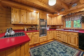 A wooden cabin interior with a red countertop, stainless steel appliances, and a large window with curtains.