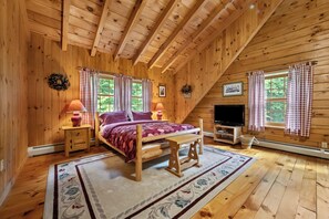 Un dormitorio de cabaña de madera acogedor, con una cama, dos lámparas de noche, un televisor y una chimenea.