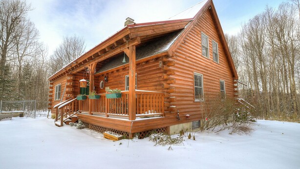 Une cabane en rondins avec un porche en bois, une cheminée et un paysage enneigé.