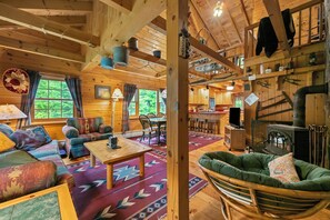A cozy cabin interior with a dining area, a sofa, a fireplace, and a kitchen visible through an open door.